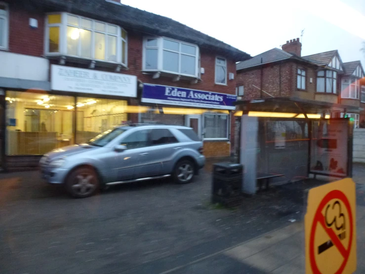 a silver car driving past a sidewalk sign