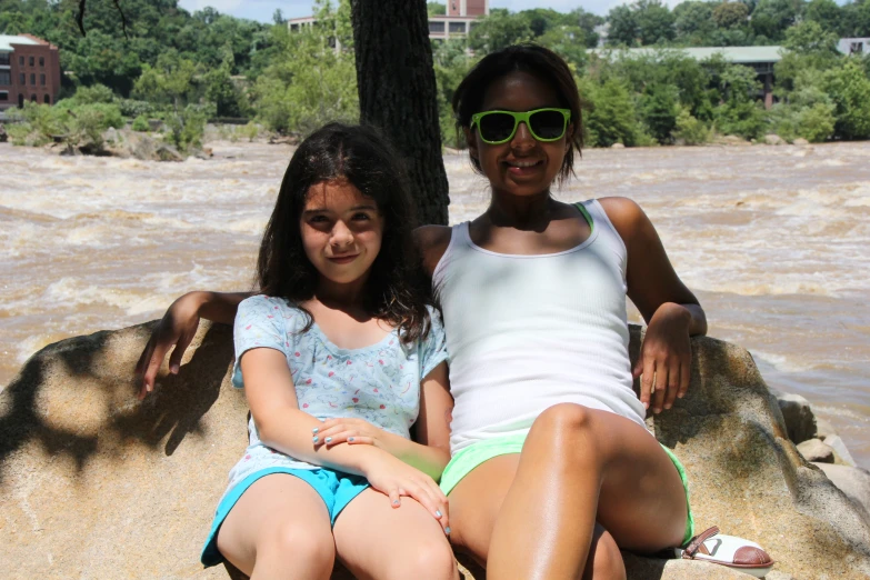 a couple of girls sitting next to each other on a rock