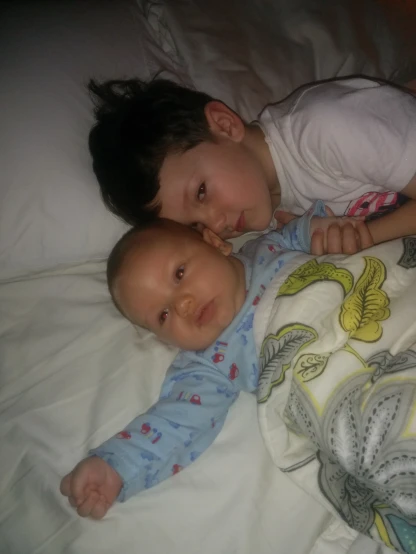 two children laying in bed looking at the camera