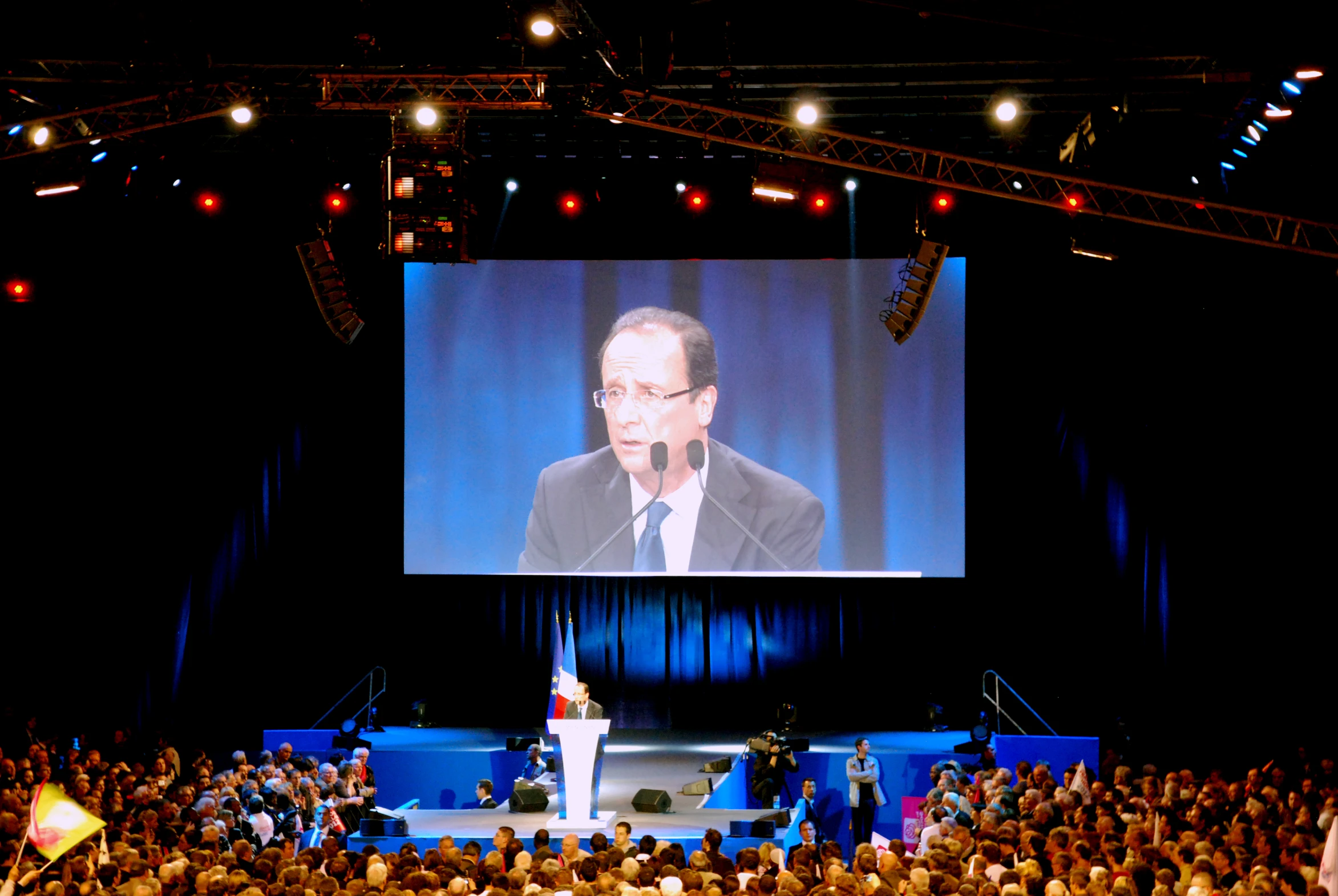 a large crowd is watching a speaker on a big screen