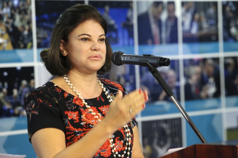 a woman wearing a colorful top speaks from a podium