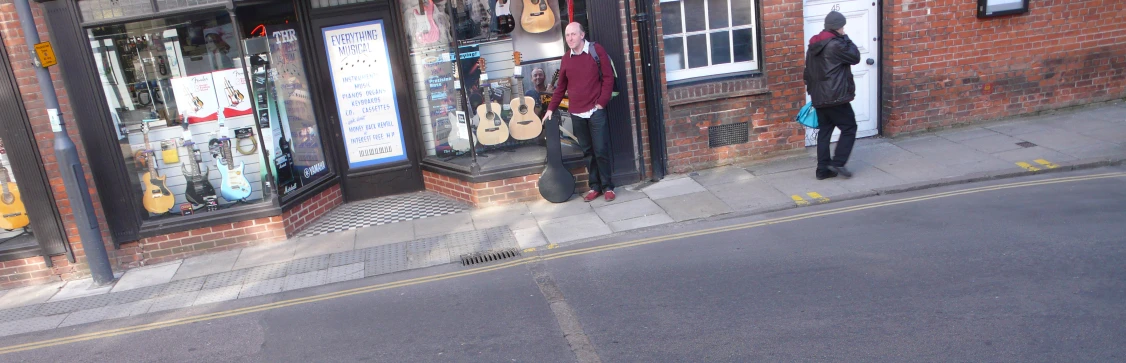 a man standing outside a music store with a guitar hanging from the wall