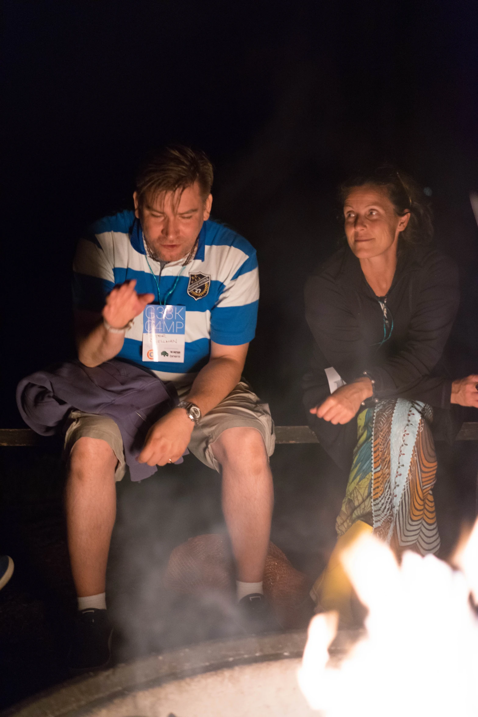 a couple sit together next to a campfire