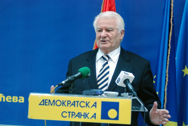 an old man standing in front of a podium with microphones