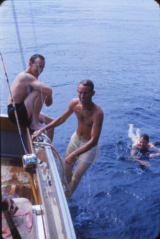 two men swim off of a boat near a person swimming