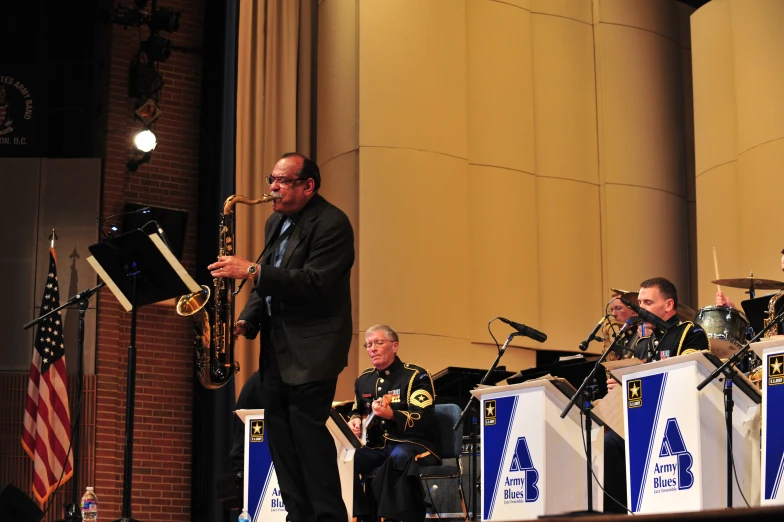 a man with glasses plays on a trumpet while three men look to his left