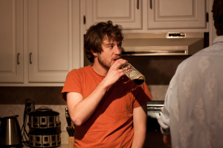 a man drinking from a cup while in a kitchen