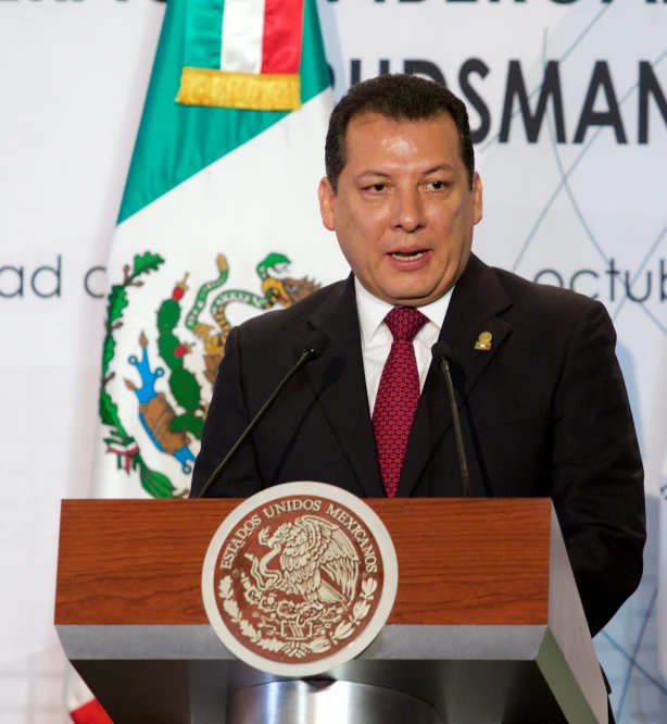 a man standing at a podium with flags in the background