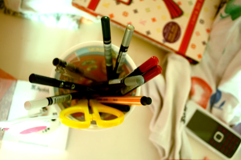 a cup filled with markers and pens sits on a table