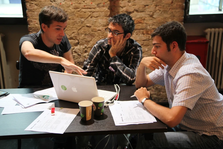 three guys sitting at a table working on soing