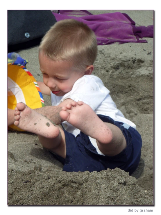a boy on a beach in the sand with his feet up