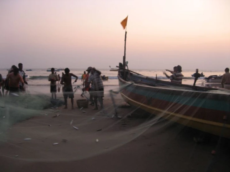 many people standing by boats on a beach near the water