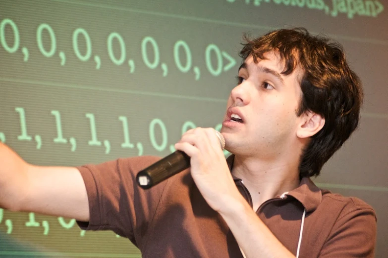 a man speaking into a microphone in front of a projection screen