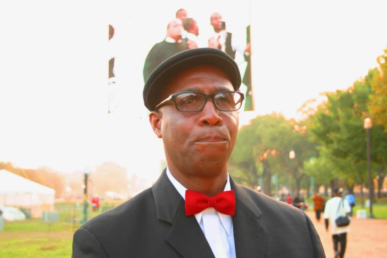 a man wearing a hat and glasses standing in front of trees