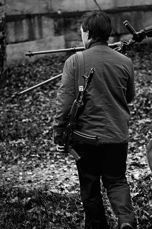 black and white pograph of man carrying an ar - 15 rifle to a shooting range