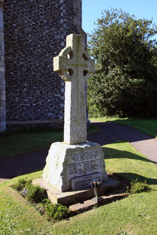 a cement cross standing in the middle of some grass