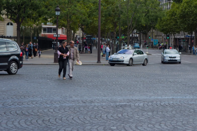 two people crossing the street in front of parked cars