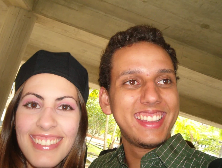 a man and woman smiling at camera while standing under an awning