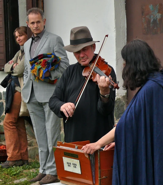 a man playing violin next to a woman in a cape