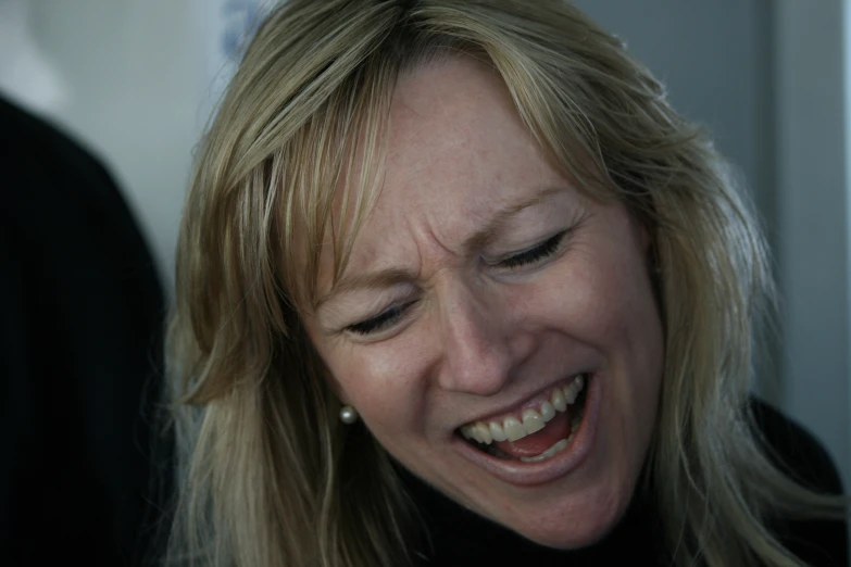 a smiling blonde woman wearing a pearl necklace