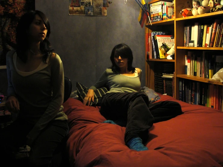 two young women sitting on a bed, one looks up