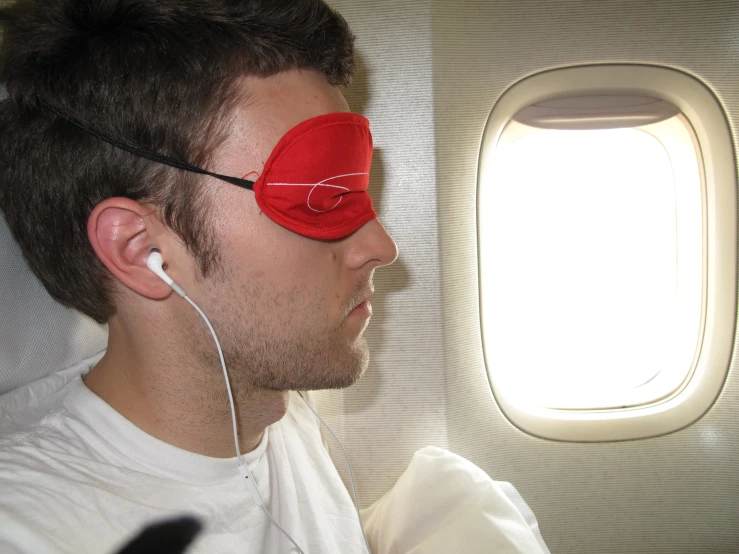 a man with a mask on, sitting beside an airplane window