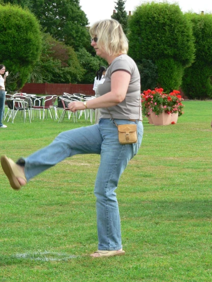 a woman wearing jeans and sandals kicking an object in the grass