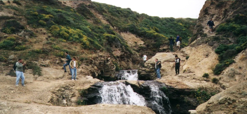 a group of people standing on the side of a cliff next to a waterfall