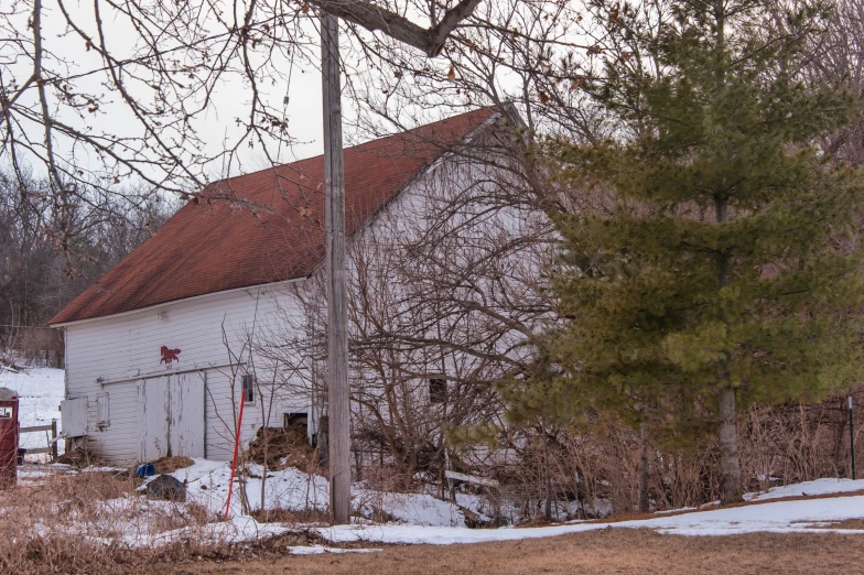 a barn with snow on the ground and tree behind