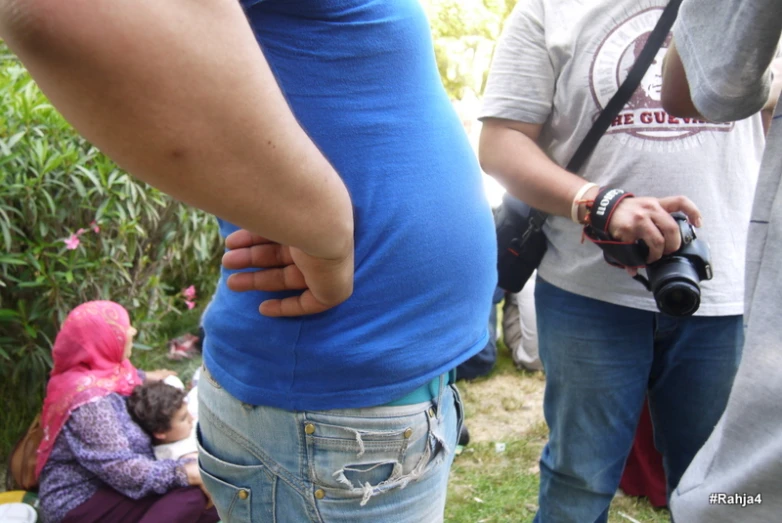 people standing around and sitting in the grass, with children playing around them