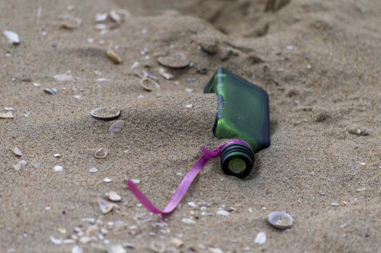 an empty bottle on top of a beach with a ribbon