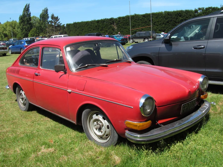 old, rusted, red car in grassy field next to other cars