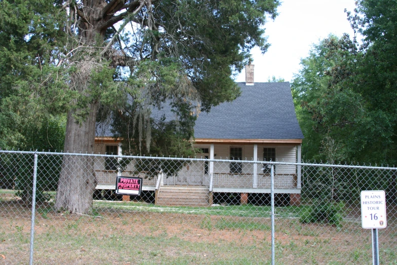 a house with a sign on the fence, next to a tree