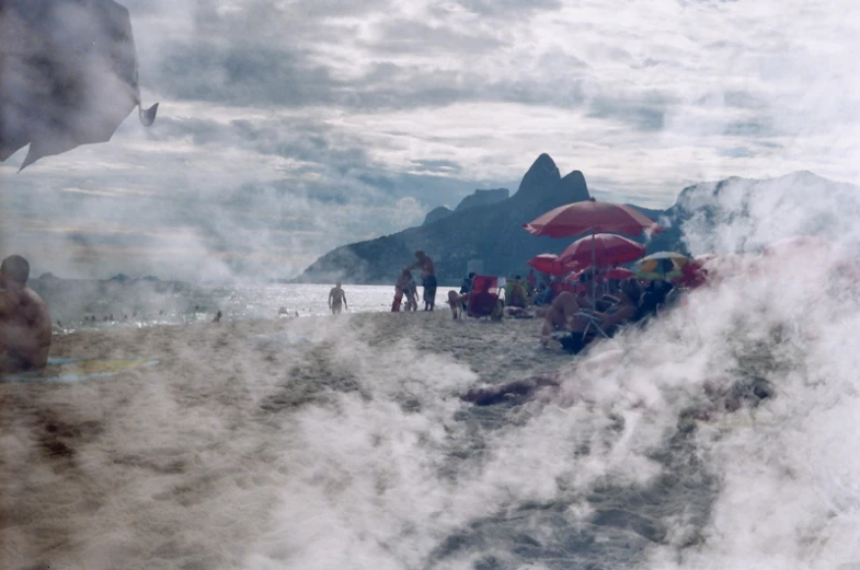 people are standing on the beach, in front of the mountains