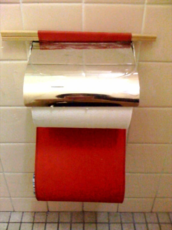 a red toilet paper holder with a roll of silver foil on top of it