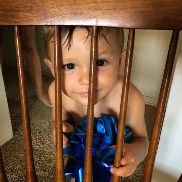 baby looking through bars at himself with a blue bow on it