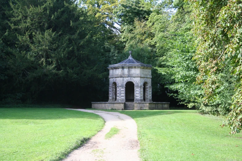 an open area with a stone gazebo and path through the grass