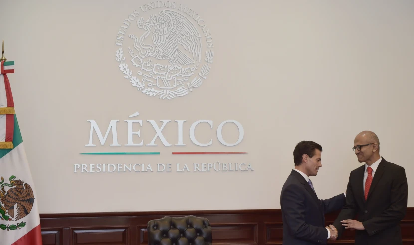 two men shaking hands in front of a mexican flag