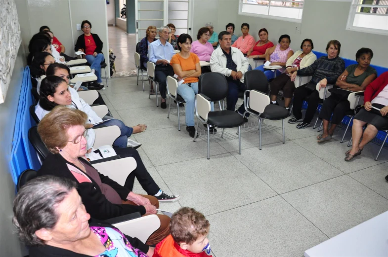 large group of people sitting in chairs, watching an exhibit