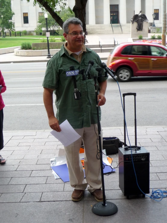 man in green shirt with microphone and microphone stand on sidewalk