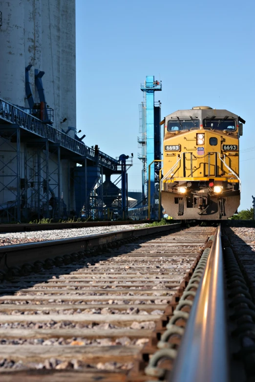 an old yellow locomotive train traveling past a grain factory