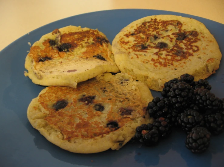 three pancakes with some blackberries on a blue plate