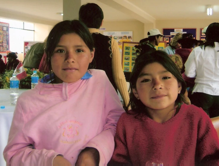 two s sitting in front of a camera in a room full of people