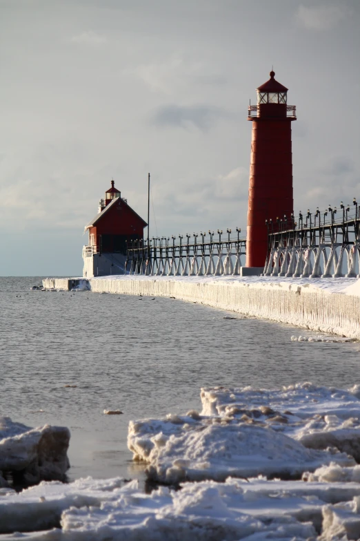 a snowy shore line has a red and white light house next to the ocean