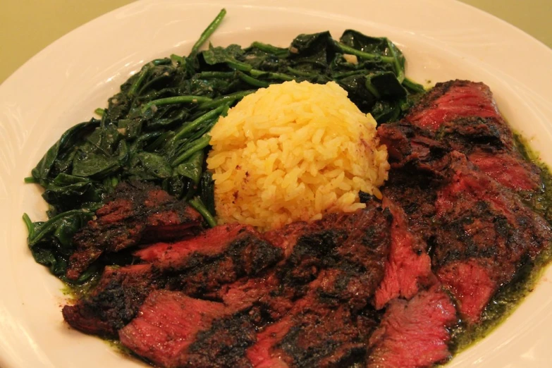 steak and spinach with a yellow rice on the plate