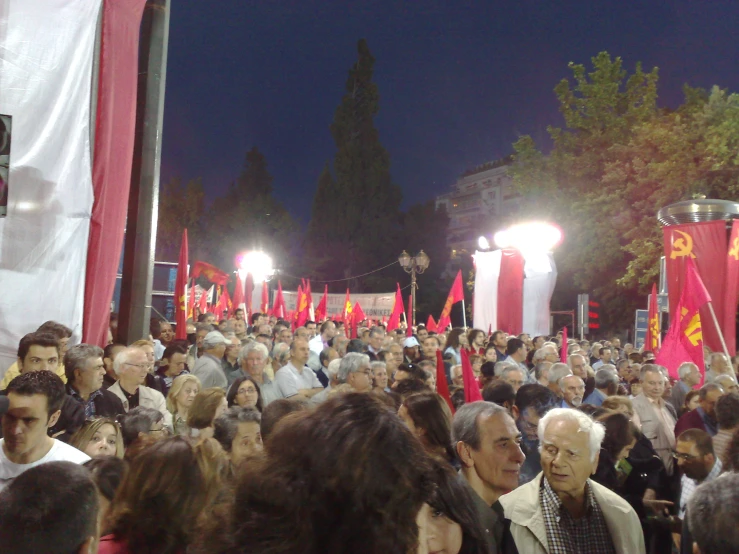 a crowd of people walking past red flags and banners