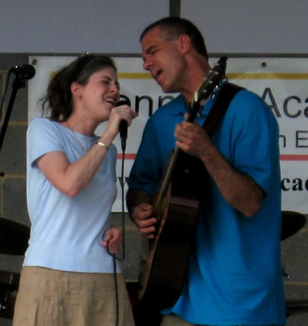 the woman singing into a microphone next to a man with an acoustic guitar