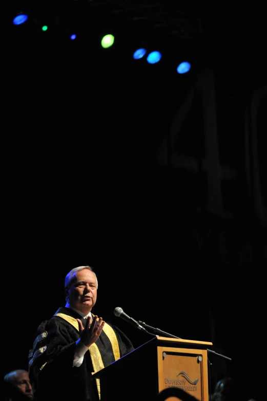 a man standing at a podium with his hands up and giving a speech