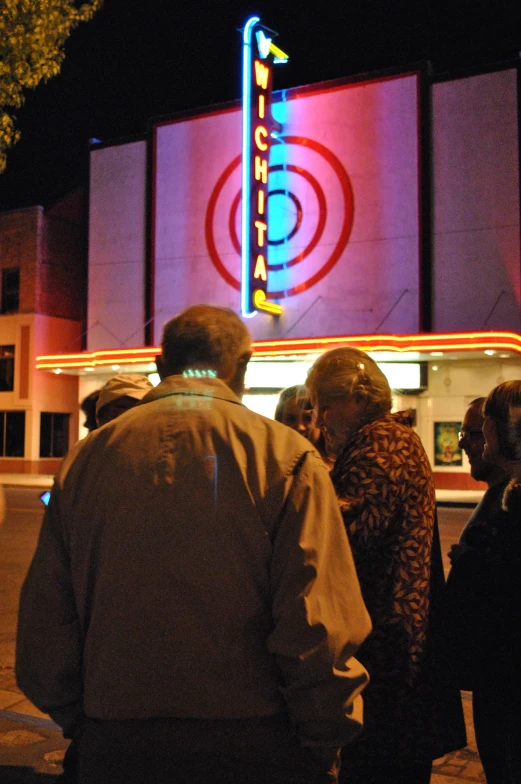 a group of people gathered outside of a theater at night