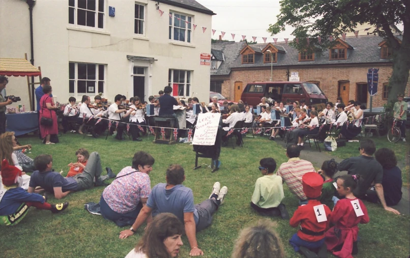 a large group of people gathered on the grass to listen to the band